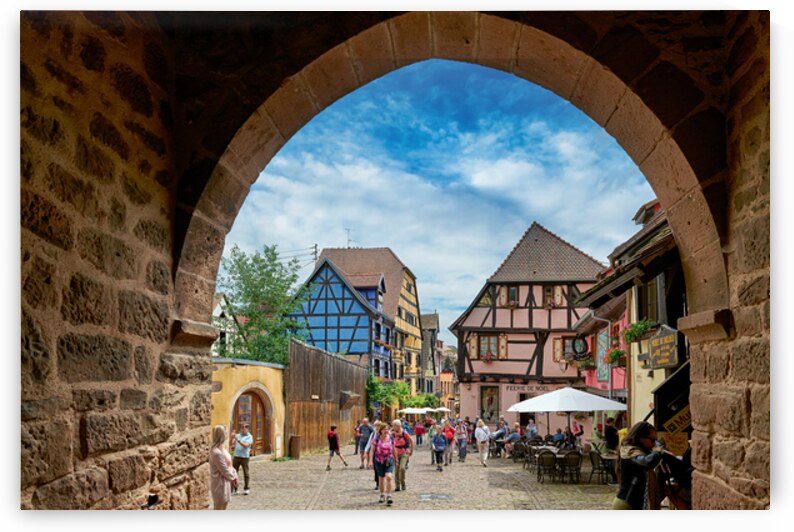 Visitors explore Riquewihr with timber framed houses under blue  by Marco Brivio