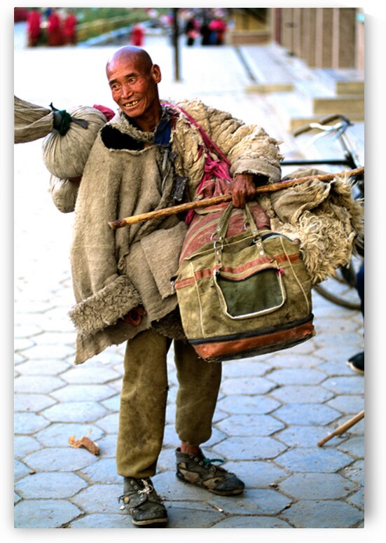 Smiling man carries bundles while walking on street in Tibet by Marco Brivio