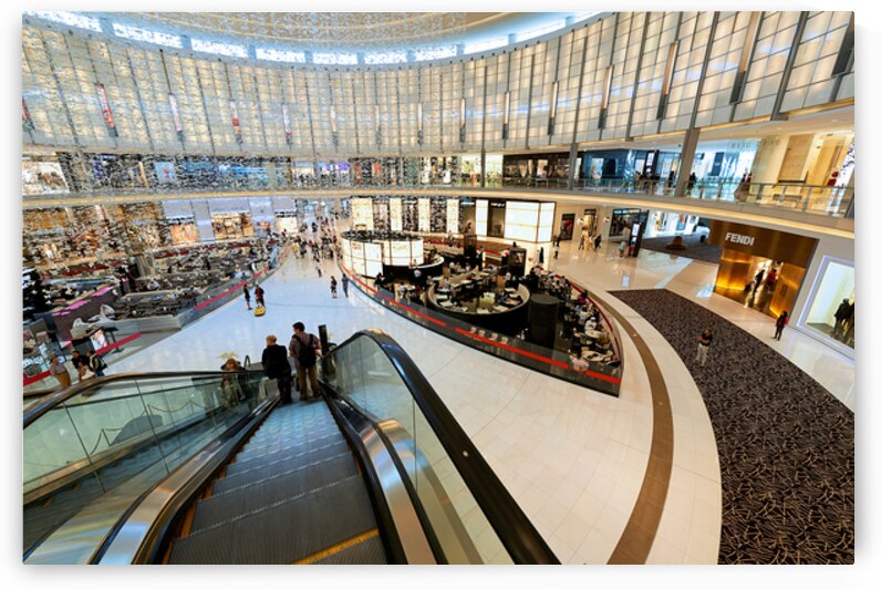 Busy shopping mall in Dubai with escalators and various stores by Marco Brivio