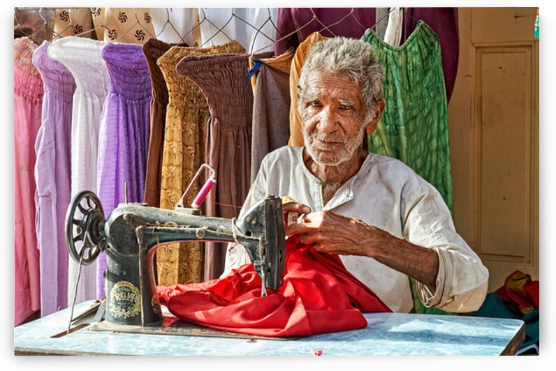 Elder man sewing red fabric in Jaisalmer Rajasthan India by Marco Brivio