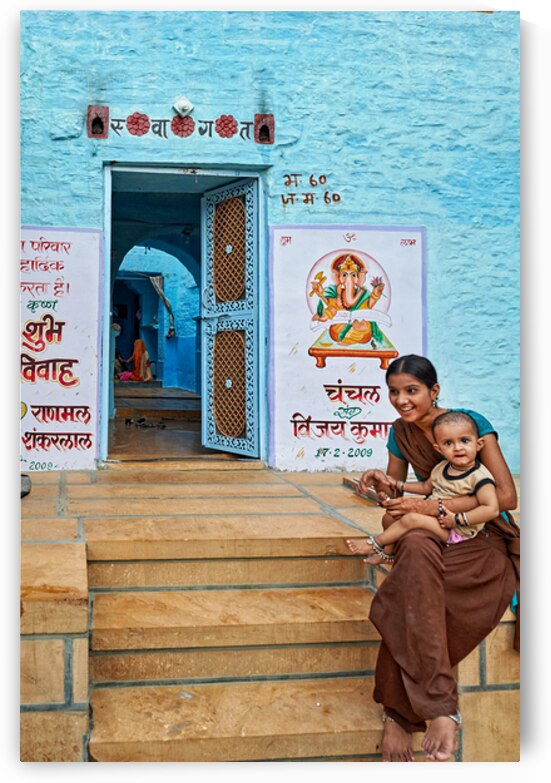 Mother and son sit on steps near a blue building in Jaisalmer by Marco Brivio