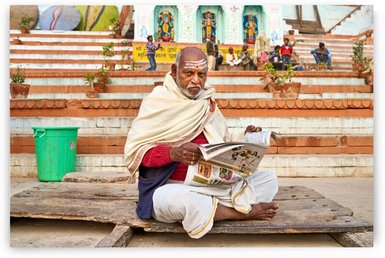 Man reads newspaper by river in Varanasi India by Marco Brivio