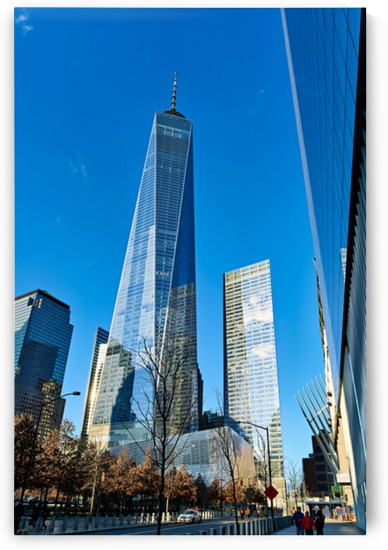 People walk near One World Trade Center with clear blue sky abov by Marco Brivio