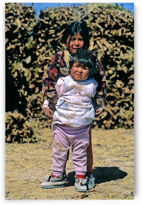 Two indigenous children one holding another outdoors. by Marco Brivio