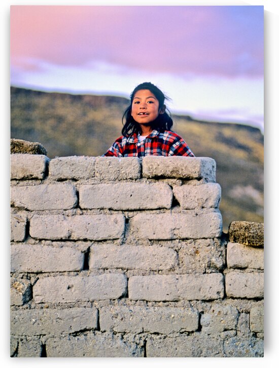 Young girl smiles over stone wall at sunset. by Marco Brivio