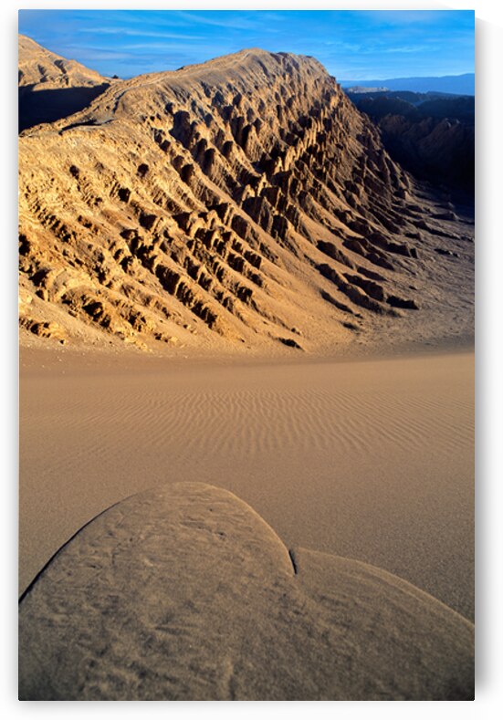 Eroded desert mountains and rippled sand under blue sky. by Marco Brivio