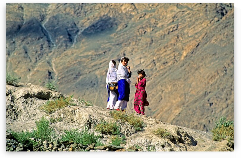 Women walk on hillside in Pakistan with mountains in view by Marco Brivio