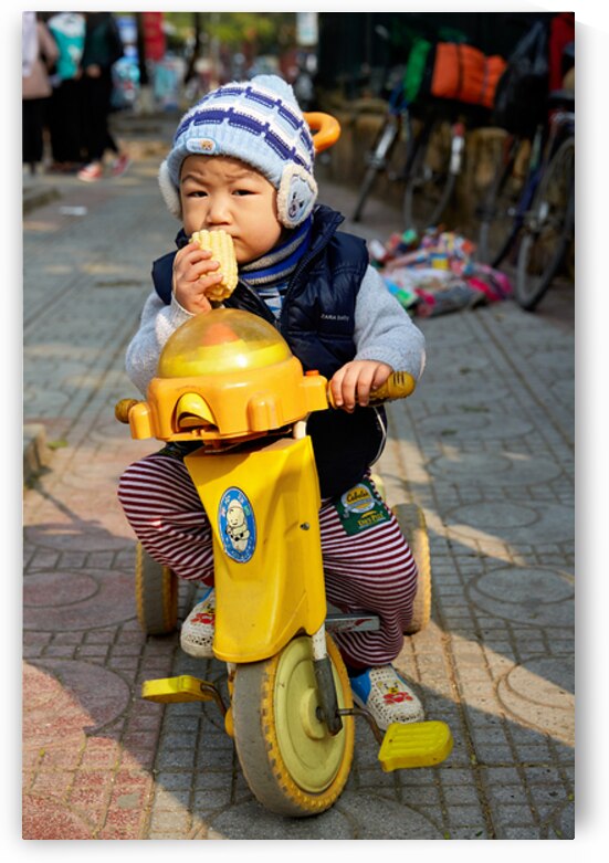 Child enjoys snack while riding tricycle in Hanoi streets by Marco Brivio