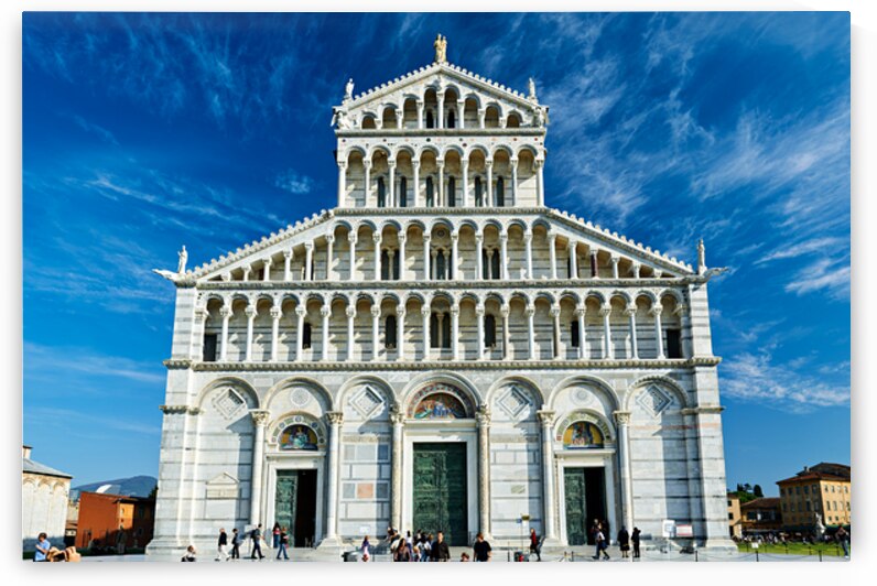 Visitors walk around Pisa Cathedral in Piazza dei Miracoli. The tall structure stands under a blue sky. People enjoy the lively atmosphere. by Marco Brivio