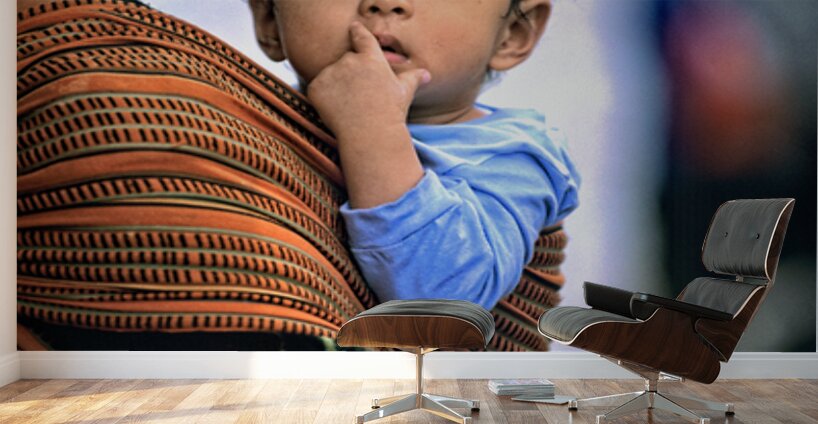 Curious child carried in a patterned fabric sling. Wall Murals