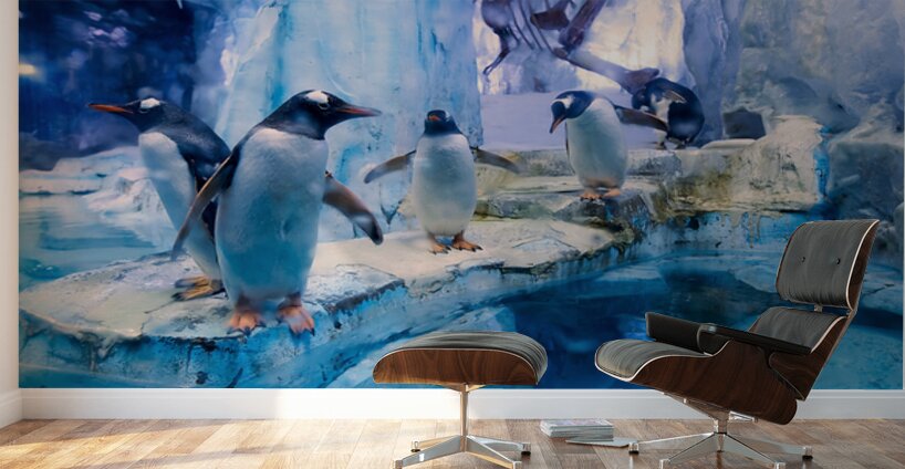 Penguins play on ice near water with a skeleton exhibit in Dubai Wall Murals