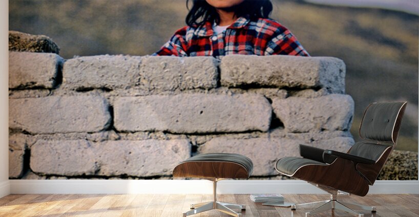Young girl smiles over stone wall at sunset. Wall Murals