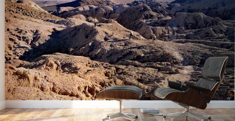 Hikers traverse a vast arid rocky desert landscape. Wall Murals