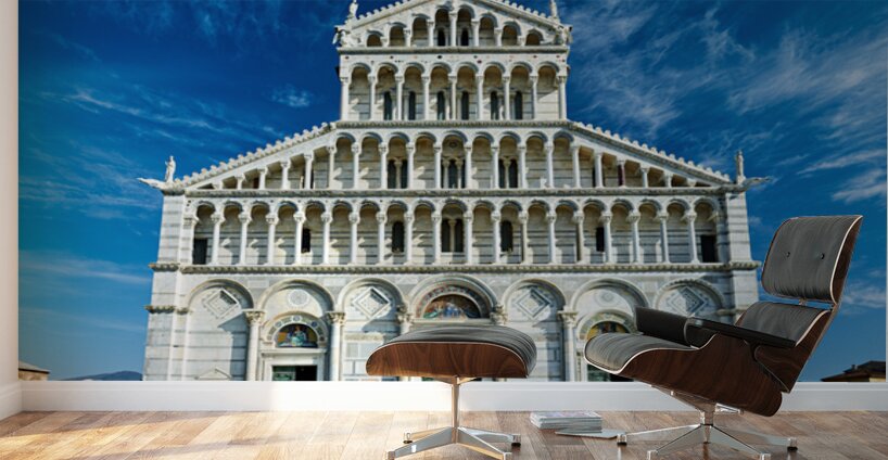 Visitors walk around Pisa Cathedral in Piazza dei Miracoli. The tall structure stands under a blue sky. People enjoy the lively atmosphere. Wall Murals