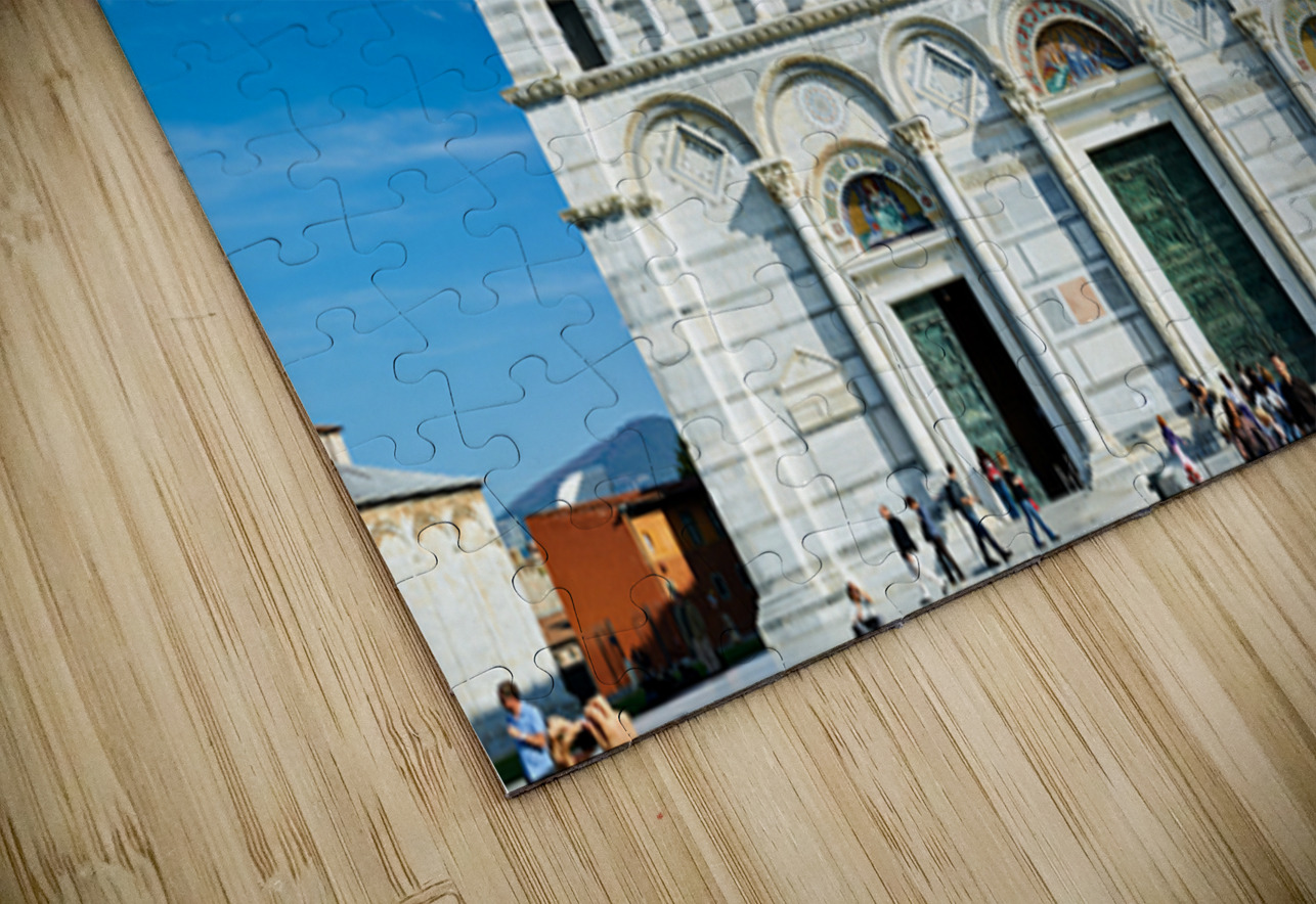 Visitors walk around Pisa Cathedral in Piazza dei Miracoli. The tall structure stands under a blue sky. People enjoy the lively atmosphere. Marco Brivio Puzzle