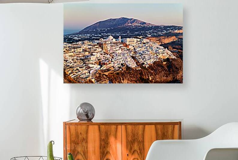 Santorini cliffside town at sunset with mountain backdrop. by Marco Brivio