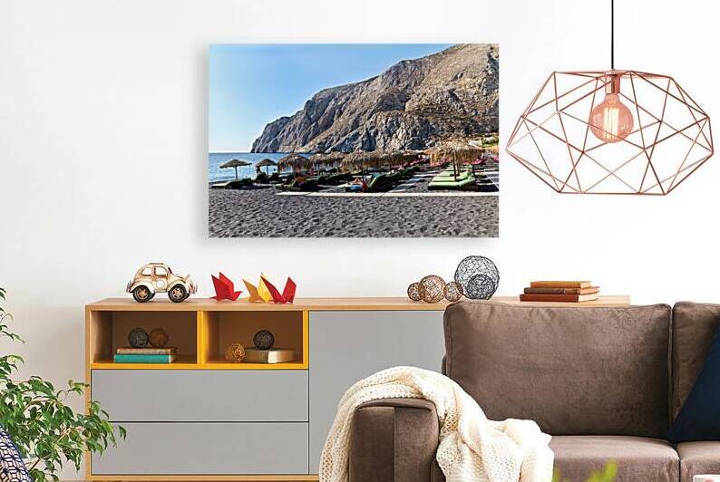 Beachgoers relax on black sand beach under straw umbrellas. by Marco Brivio