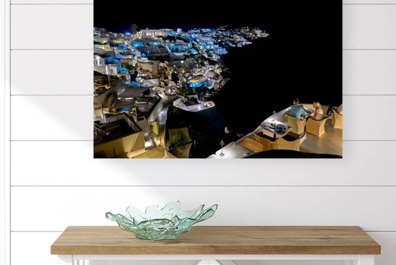 Illuminated cliffside town at night couple enjoying dinner. by Marco Brivio