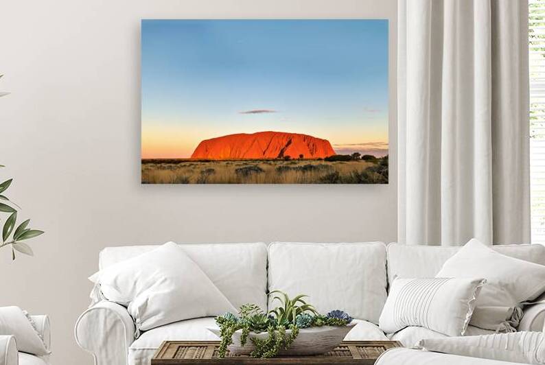 Uluru glows orange at sunset under a clear blue sky. by Marco Brivio