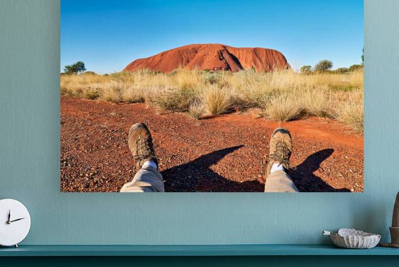 Persons feet in hiking boots in front of Uluru. by Marco Brivio
