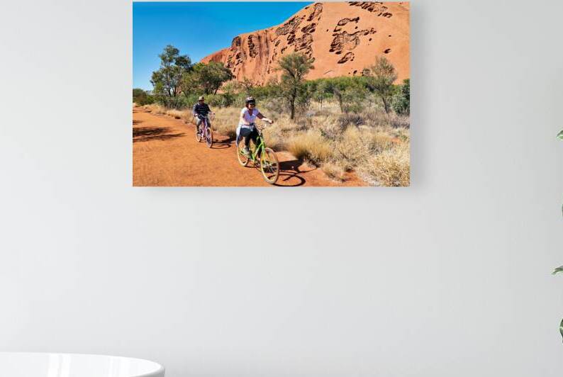 Two people cycling near Uluru under a clear blue sky. by Marco Brivio