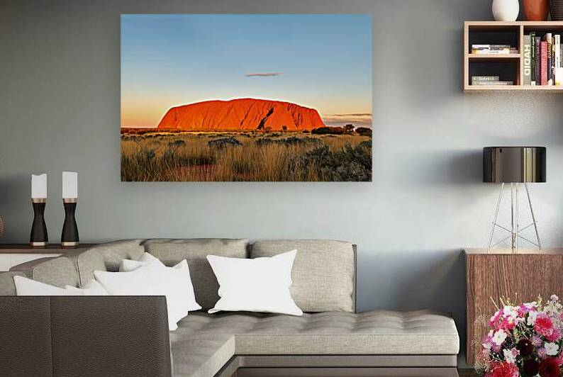 Uluru glows orange at sunset with a vast grassy plain. by Marco Brivio