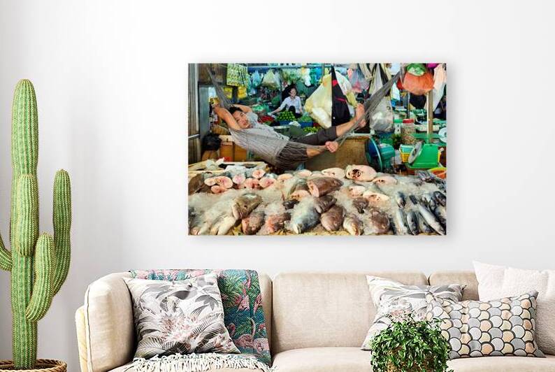 Market vendor relaxes in hammock above fresh fish. by Marco Brivio