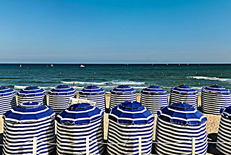 Beach scene in Cabourg Normandy with striped umbrellas on sand by Marco Brivio