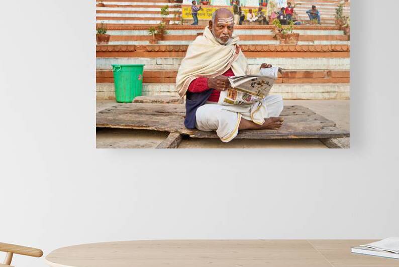 Man reads newspaper by river in Varanasi India by Marco Brivio