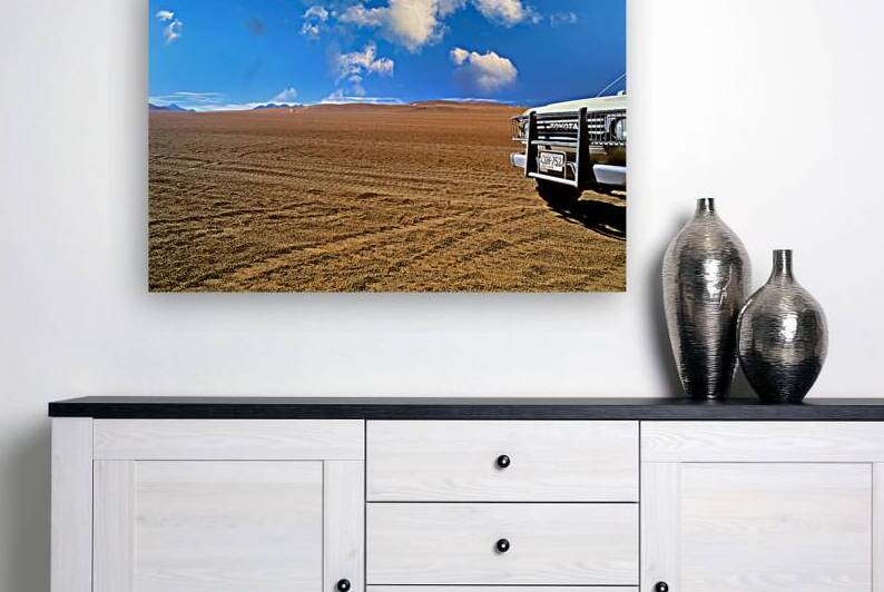 Toyota truck in vast empty desert under blue sky. by Marco Brivio