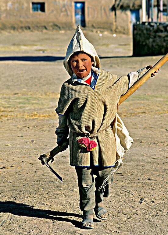 Indigenous boy with tools walks through a dusty village. by Marco Brivio