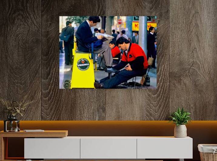 Man gets shoes shined while reading newspaper on street. by Marco Brivio