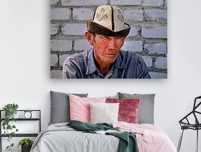 Man in traditional hat sits against a brick wall in Bukhara by Marco Brivio
